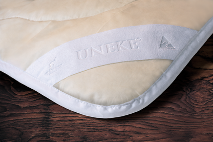 Close-up of a beige and white mattress pad with 'UNIKET' branding on a wooden surface.