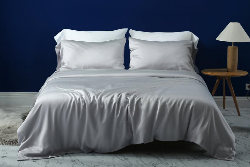 Bed with white bedding against a dark blue wall with a side table and lamp.